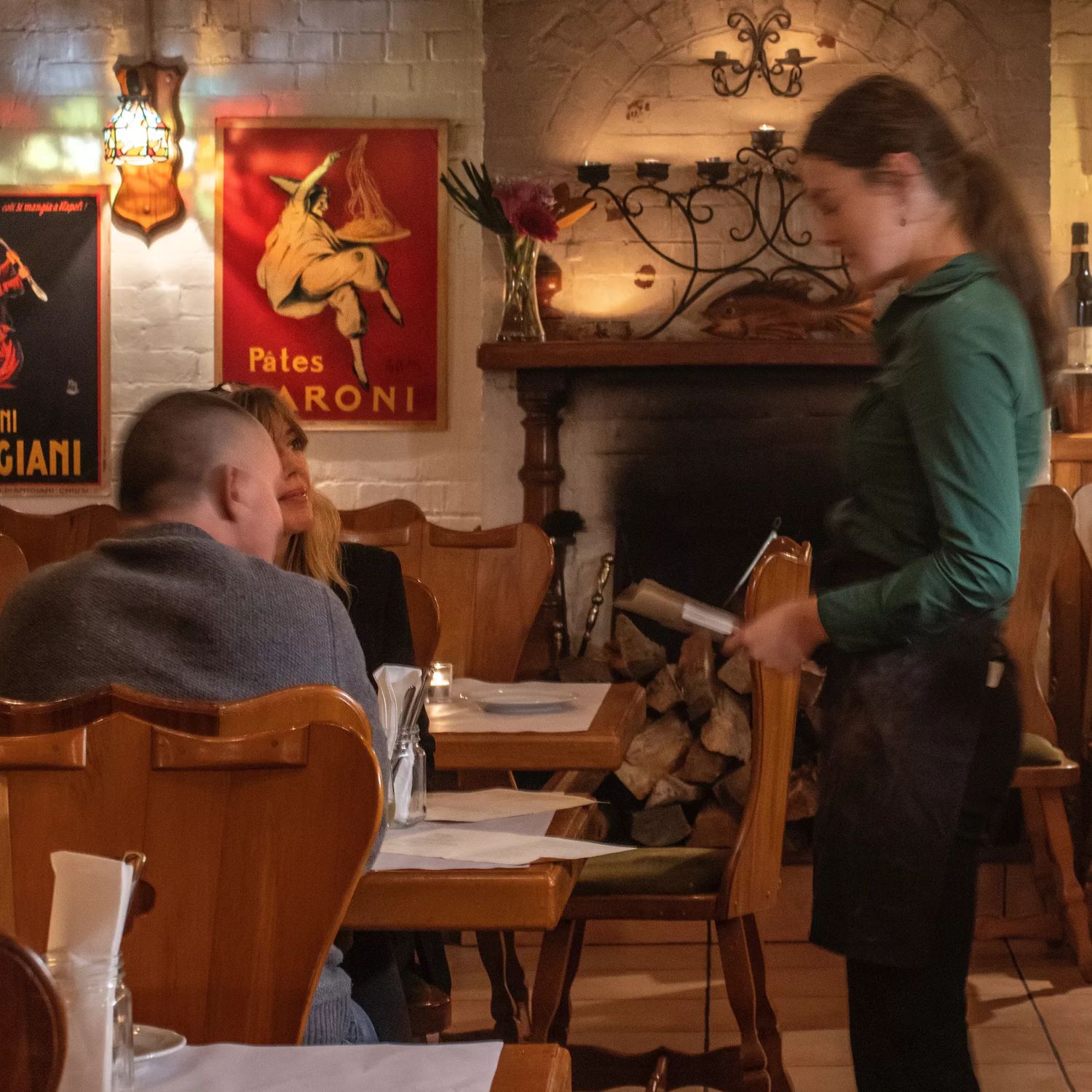 Waiter inside Cicio Cacio serving a table of customers with dim mood lighting and wooden fixtures surround.
