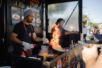 Chefs in a truck at the Harbourside Markets flame cooking noodles.