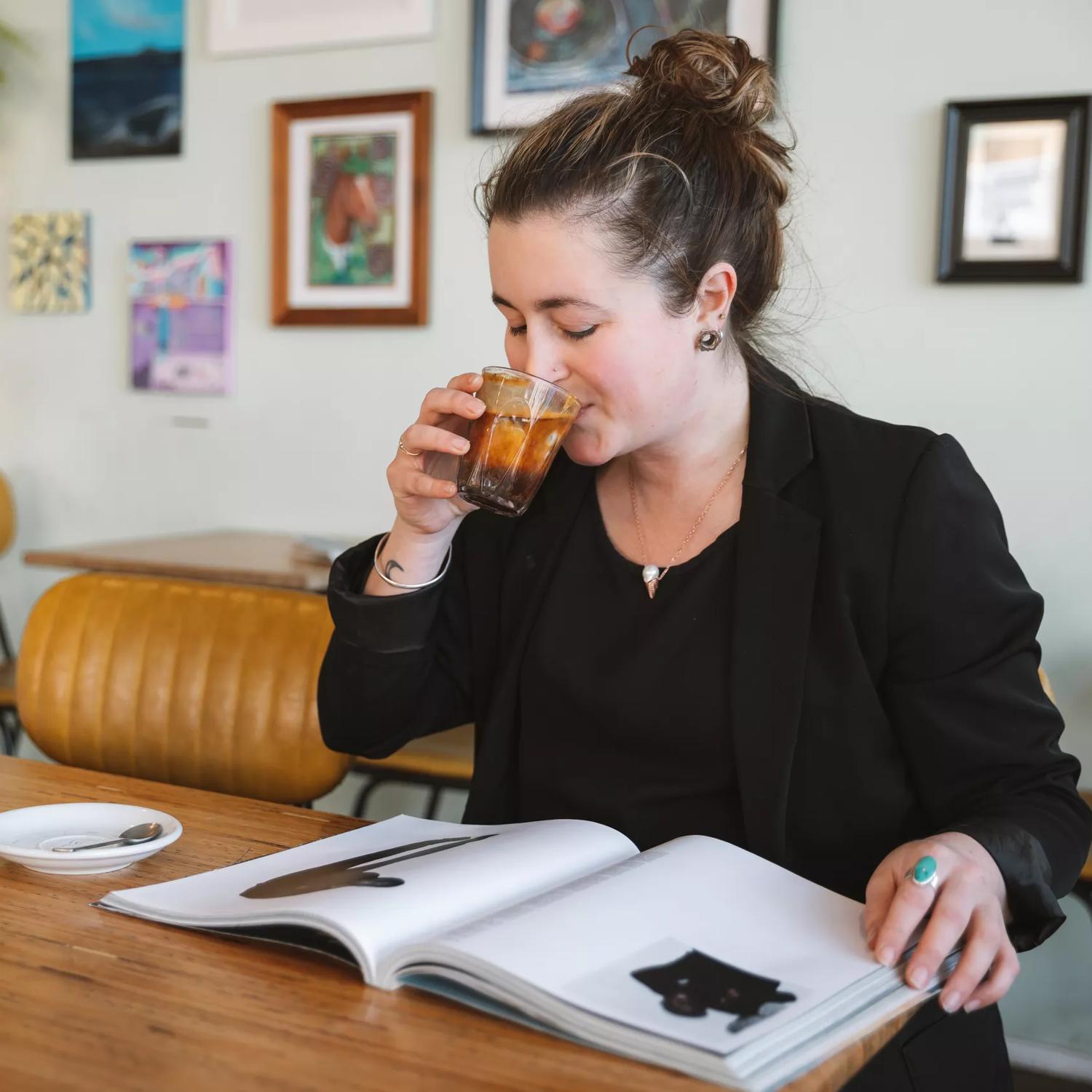 A person drinks a coffee while reading a book at Swimsuit Coffee, a café in Te Aro, Wellington.