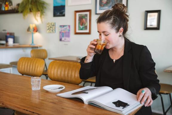 A person drinks a coffee while reading a book at Swimsuit Coffee, a café in Te Aro, Wellington.