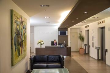 A modern hotel lobby with a small leather couch, a smiling concierge sitting at the desk and elevator doors on the right side.