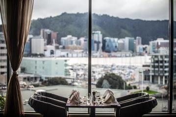 The view from the Copthorne Hotel dining room, 4 chairs sit at a table right next to a floor to ceiling window, overlooking the waterfront and Wellington harbour.