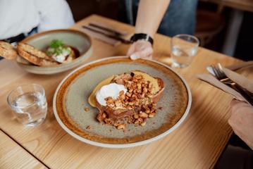 Close-up of hand placing a plate of tsoureki french toast on the table at August Eatery in Wellington.