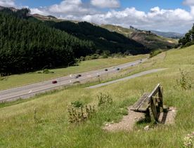 A wooden bench on a grassy hill overlooking a highway.