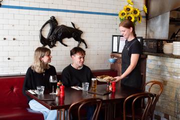 A waitress brings dishes to a couple sitting at a booth table at El Matador.