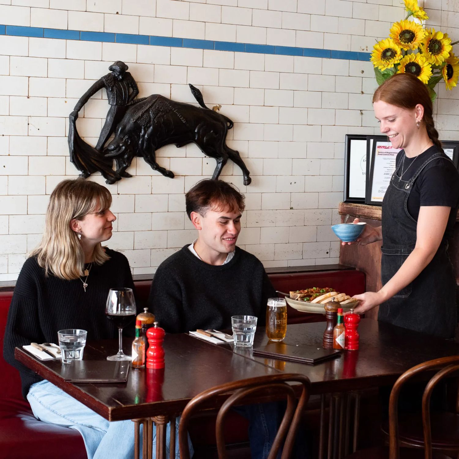 A waitress brings dishes to a couple sitting at a booth table at El Matador.