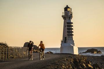 2 bikers on the Pencarrow Coast Road at sunset, with the lighthouse in the background.