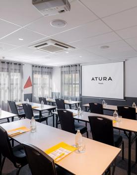 Conference room inside Atura Hotel with 6 tables facing a projector.