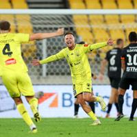 David Ball, an attacker on the Wellington Phoenix FC A-league team, runs with arms wide open toward his teammate to celebrate his goal during a match.