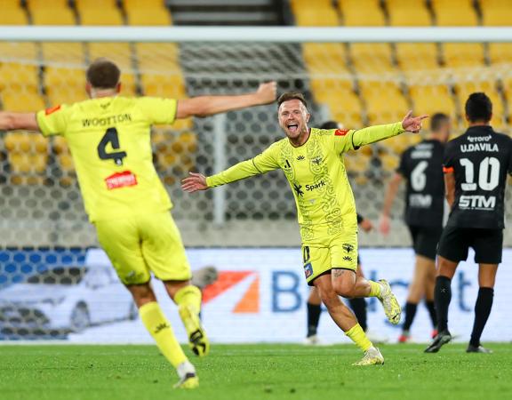 David Ball, an attacker on the Wellington Phoenix FC A-league team, runs with arms wide open toward his teammate to celebrate his goal during a match.