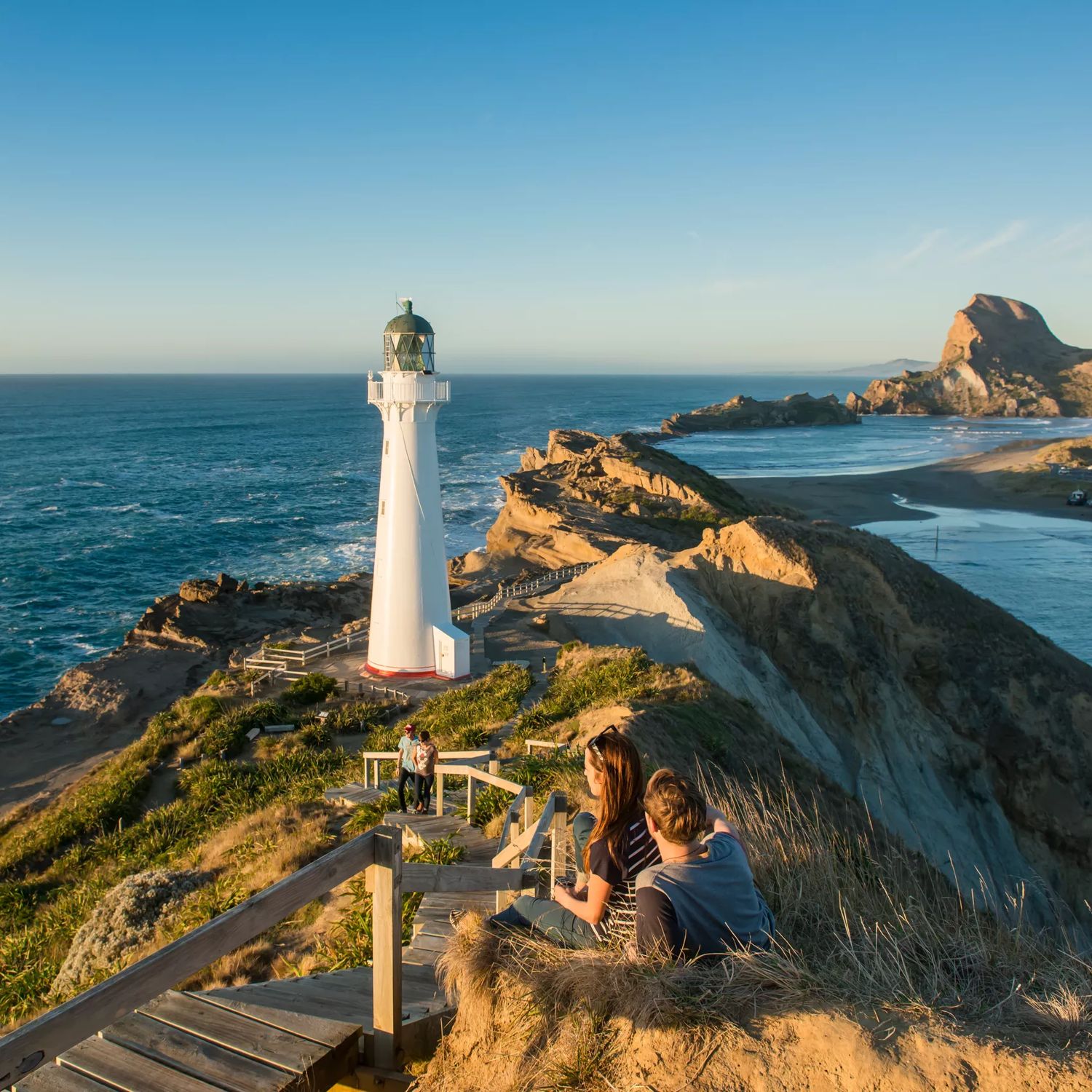 A couple sits beside the path toward Castlepoint Lighthouse to take in the view.