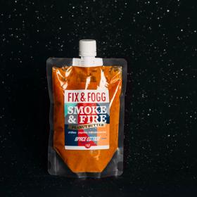 Fix & Fogg Smoke & Fire space pouch floats in space. The bright orange peanut butter is in a clear plastic pouch with a white plastic twist cap and a white, red, blue and grey label. 