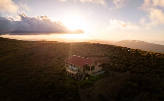 At dawn, a birdseye view of Kime Hut, a small cabin with a red roof near the top of a mountain ridge.