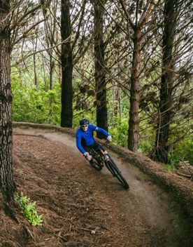 A cyclist wearing a blue jumper, helmet and sunglasses rides down a forest trail.