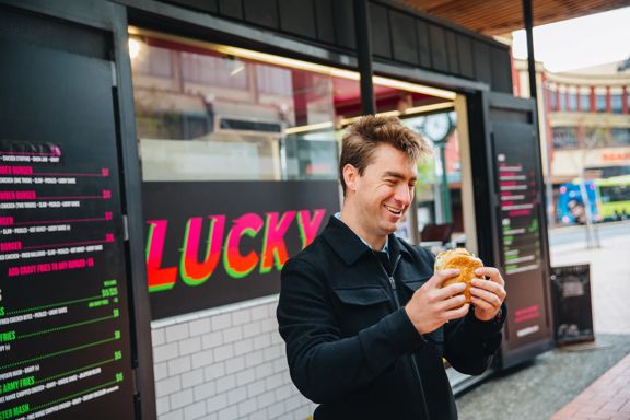 A person smiling at a burger outside Lucky on Courtenay Place