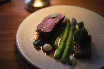 A close-up of a plate with a piece of steak, two pieces of asparagus, and dollops of white sauce.