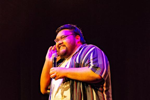 Stand-up comedian, Viki Moanan, holds a microphone while performing on stage.