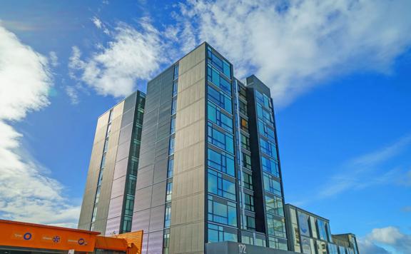 The outside of Sebel Thorndon. The hotel stands ten stories high. The sky beyond is blue with a few clouds.