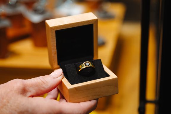 A hand holds a wooden ring box that has a Floeting diamond ring placed in it.