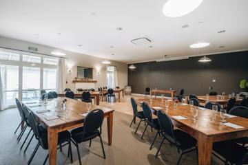 Meeting room with 5 large wooden tables, each with 7 chairs surrounding, glasses and notepads are on each table.