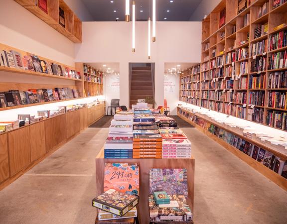 The interior of Good Books book store. A bare concrete floor with plywood shelves on either wall are filled with all sorts of books.