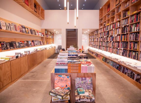 The interior of Good Books book store. A bare concrete floor with plywood shelves on either wall are filled with all sorts of books.