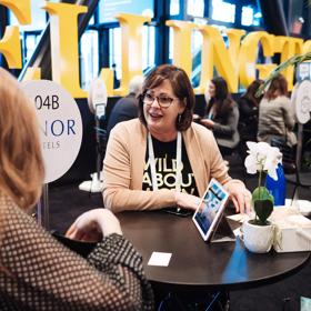 Two people talking at a small black round table at MEETINGS23, a conference created by Business Events Industry Aotearoa.