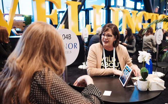 Two people talking at a small black round table at MEETINGS23, a conference created by Business Events Industry Aotearoa.