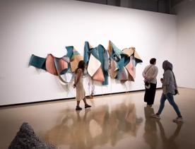 3 people standing in front of an art installation of large blue and pink colourful fabric sewn onto a wall.