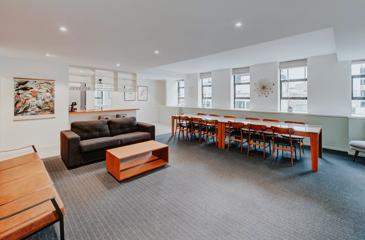 A Park Hotel suite has been set up for a boardroom meeting. It has two couches and a long table with 12 seats. In the back is the kitchen.