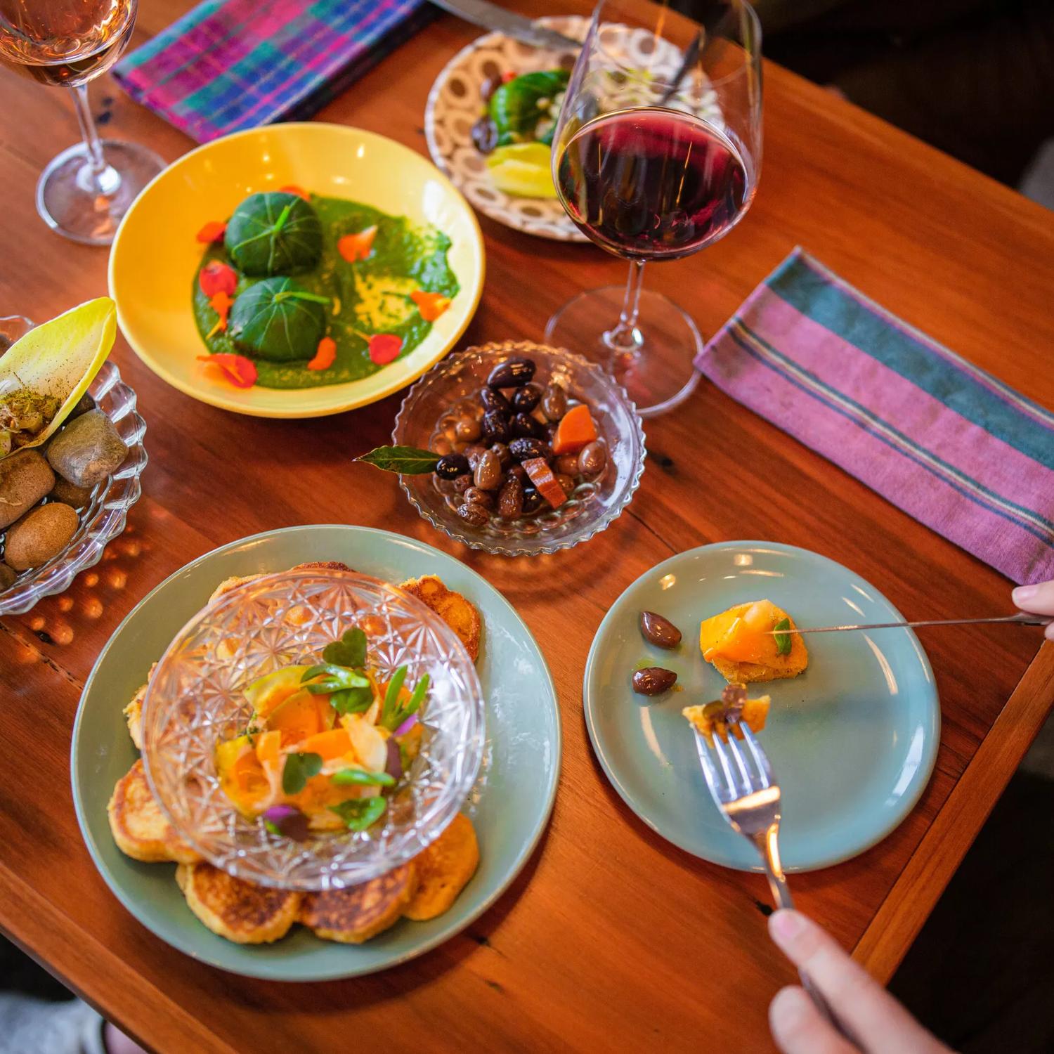 A close-up of a table with four colourful sharing plates, two glasses of wine and two side plates at Graze wine bar.