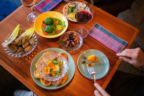 A close-up of a table with four colourful sharing plates, two glasses of wine and two side plates at Graze wine bar.