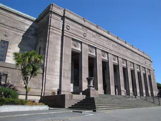 The exterior of the original Dominion Museum of New Zealand building at Massey University in Mount Cook, Wellington. The large grey building has wide pillars along the front and concrete steps leading to the entrance.