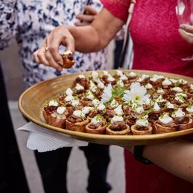 A platter of sausage roll appetizers is being handed out at an event.
