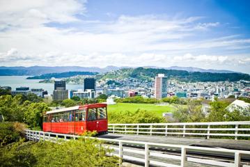 Wide look at the Cable Car driving up the tracks with Wellington city and harbour in the background