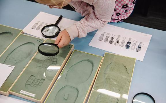 Young child looks through magnifying glass at shoe prints.