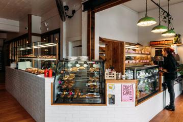 A customer waiting at the counter at Olde Beach Bakery in Paekākāriki. Three different glass cabinets contain pastries and pies.