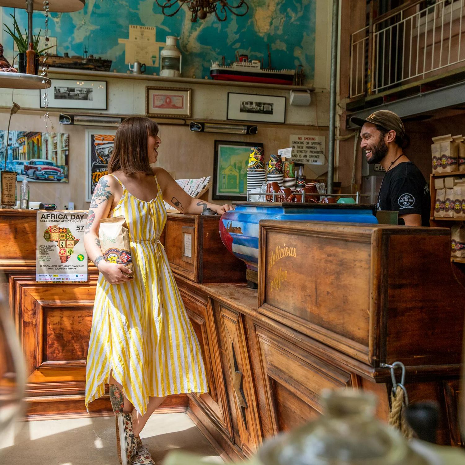 A customer and staff member laughing with eachother while the customer holds a bag of coffee beans from Havana Coffee.