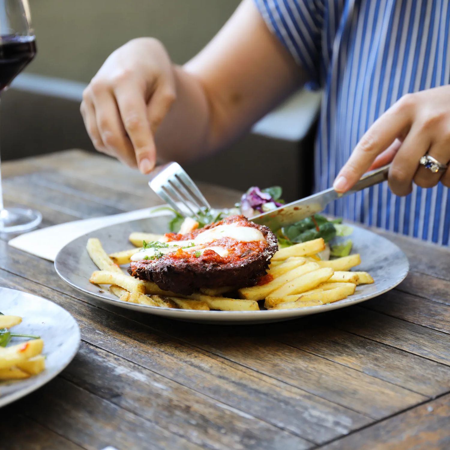 Steak and fries on a plate as a diner uses a knife and fork at a restaurant table.
