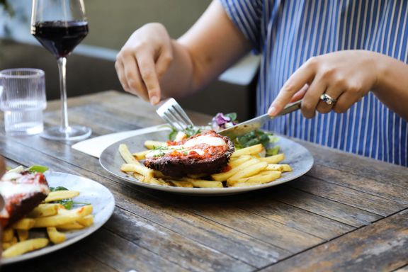 Steak and fries on a plate as a diner uses a knife and fork at a restaurant table.