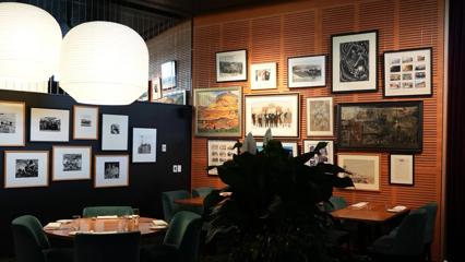 The interior of Bellamy's restaurant is inside the New Zealand Parliament building. The walls are lined with framed illustrations and photographs, and the tables are set with cutlery, water glasses and napkins.