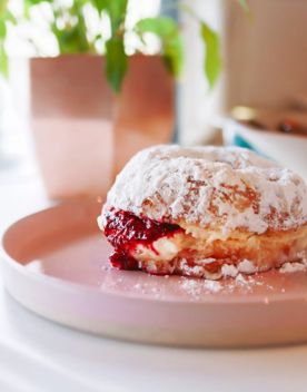 Fluffy jam and cream donut from Tomboy covered in icing sugar on a pink plate.