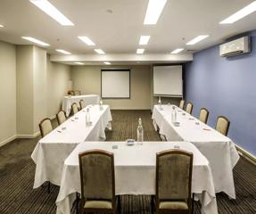 In a conference room at the Travelodge Hotel. The tables and chairs are arranged in a U-shape and have white tablecloths.