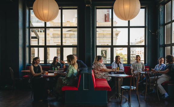 The interior seating at Regent, a cocktail pub in Te Aro Wellington, where nine patrons are seated enjoying drinks and banter.