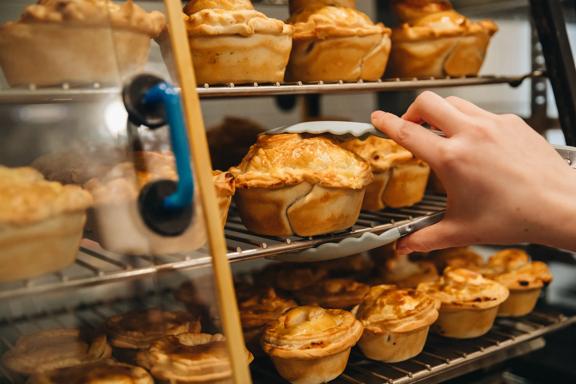 A person uses tongs to pick up a pie from a metal rack.