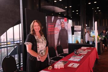 A smiling woman at the New Zealand Women in Medicine Conference 2024 stands by a red table.