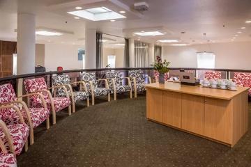 Twelve arm chairs arrangd in a semi-circle along a curved railing with a wooden counter set up wit coffee cups and a flower vase.