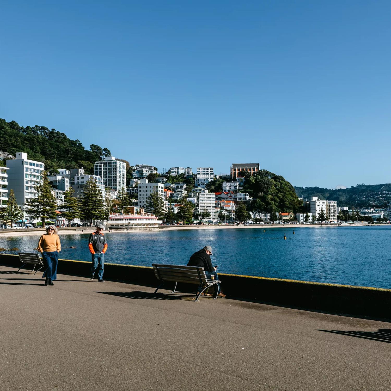 Looking towards Oriental bay with people walking along the waterfront and the fountain going in the water.