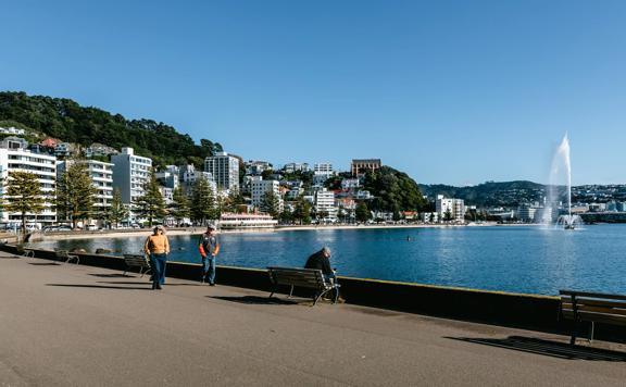 Looking towards Oriental bay with people walking along the waterfront and the fountain going in the water.