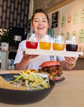 A smiling server carries a flight of craft beers to a table at Heyday Beer Co, a brewery located on upper Cuba Street in Te Aro, Wellington.